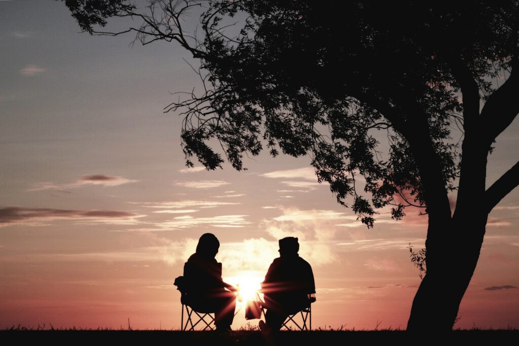 Two people sitting together under a tree at sunset